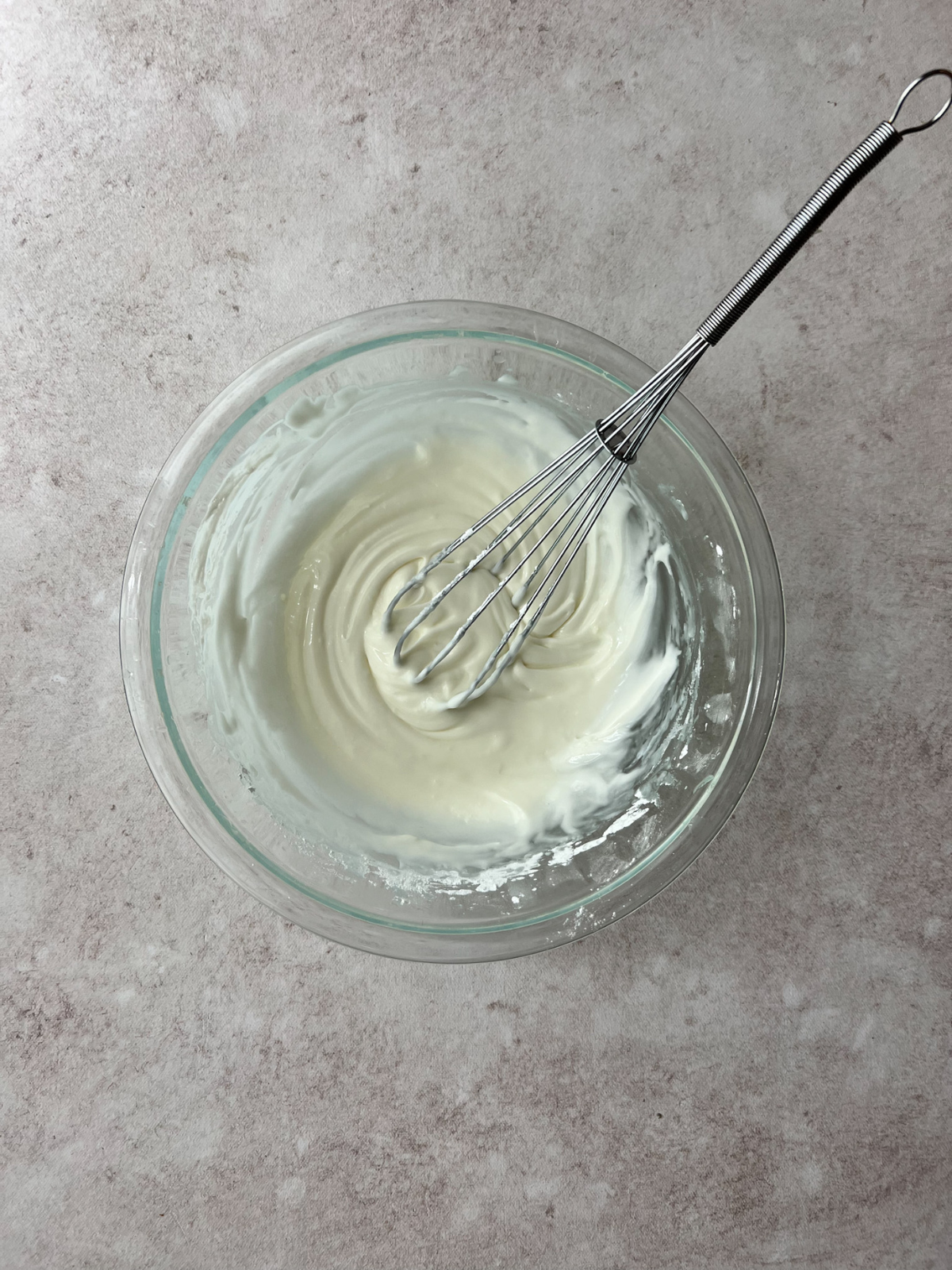 A glass mixing bowl with the key lime icing in it. A whisk sits in the bowl.