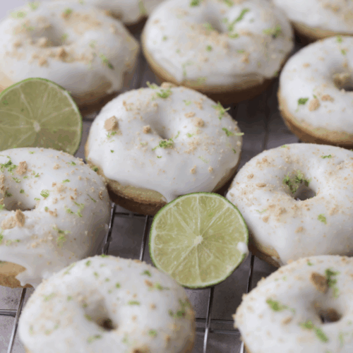 Ten key lime sourdough donuts on a wire rack adorned limes.