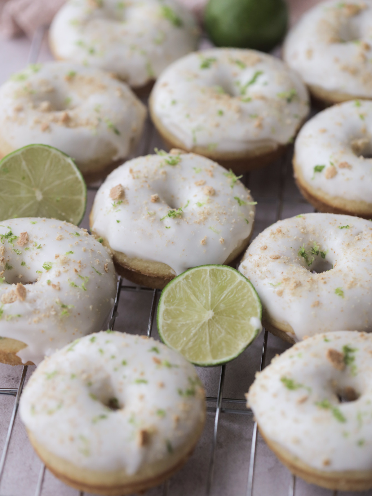 Ten key lime sourdough donuts on a wire rack adorned limes.