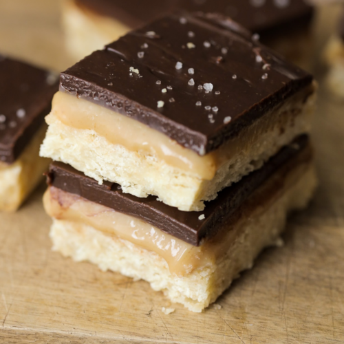 Two sourdough discard millionaire's shortbread bars stacked on top of each other. Several other bars lay in the background.