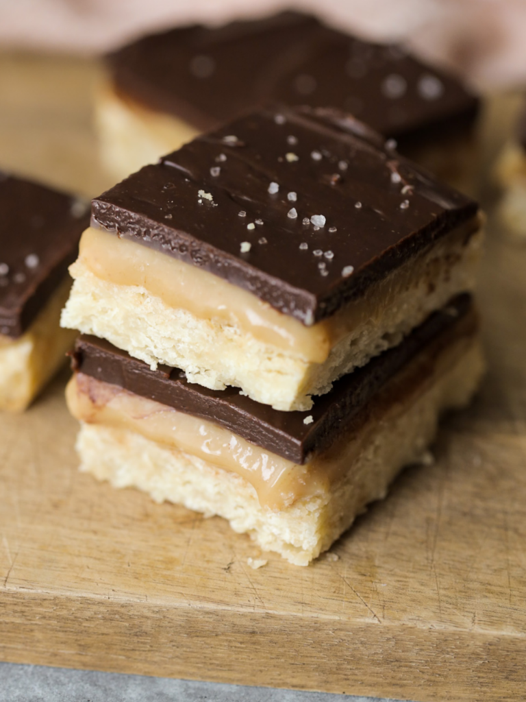 Two sourdough discard millionaire's shortbread bars stacked on top of each other. Several other bars lay in the background.