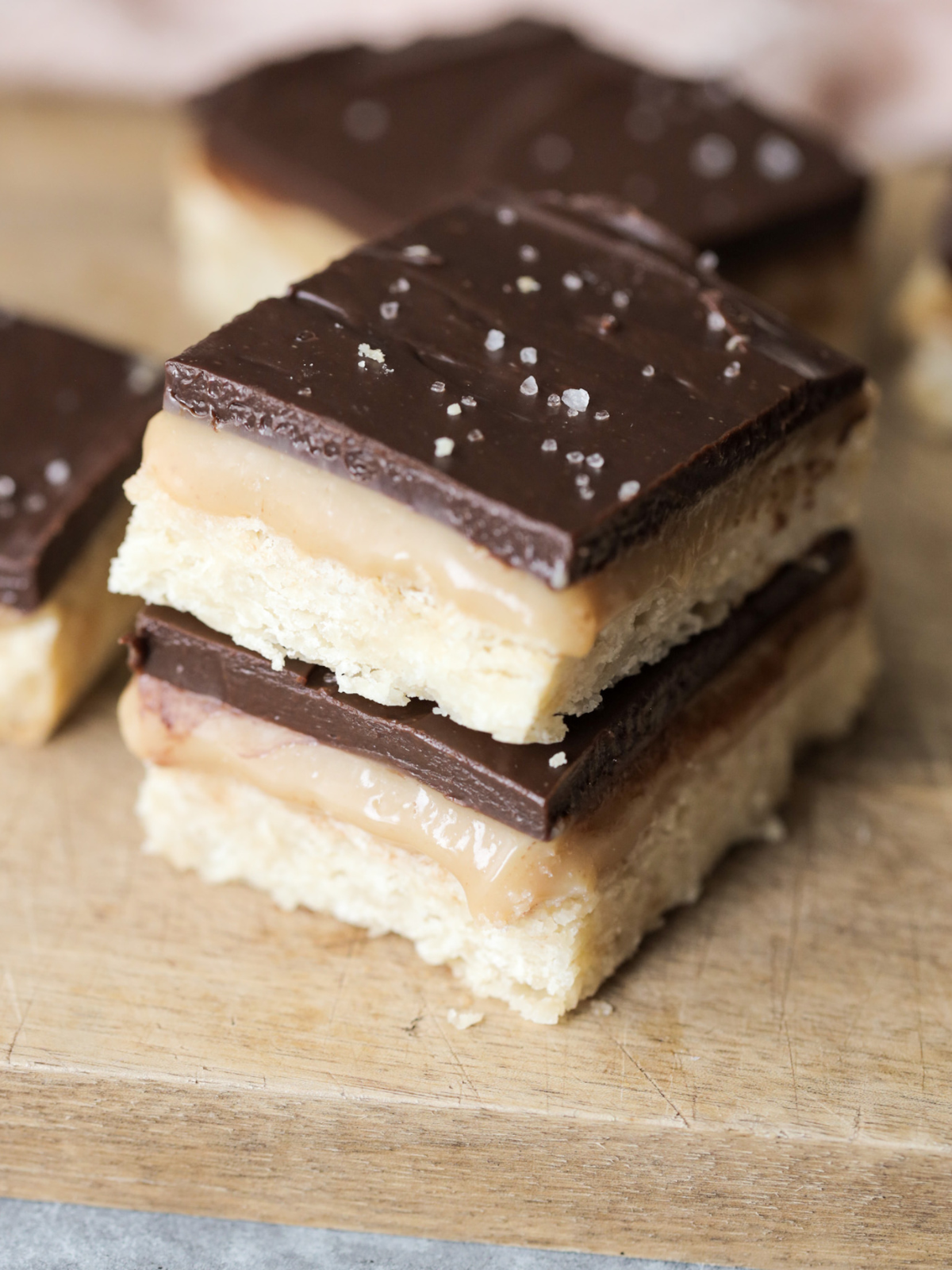 Two sourdough millionaire's shortbread bars stacked one on the other. They sit on a wooden cutting board with other bars in the background.