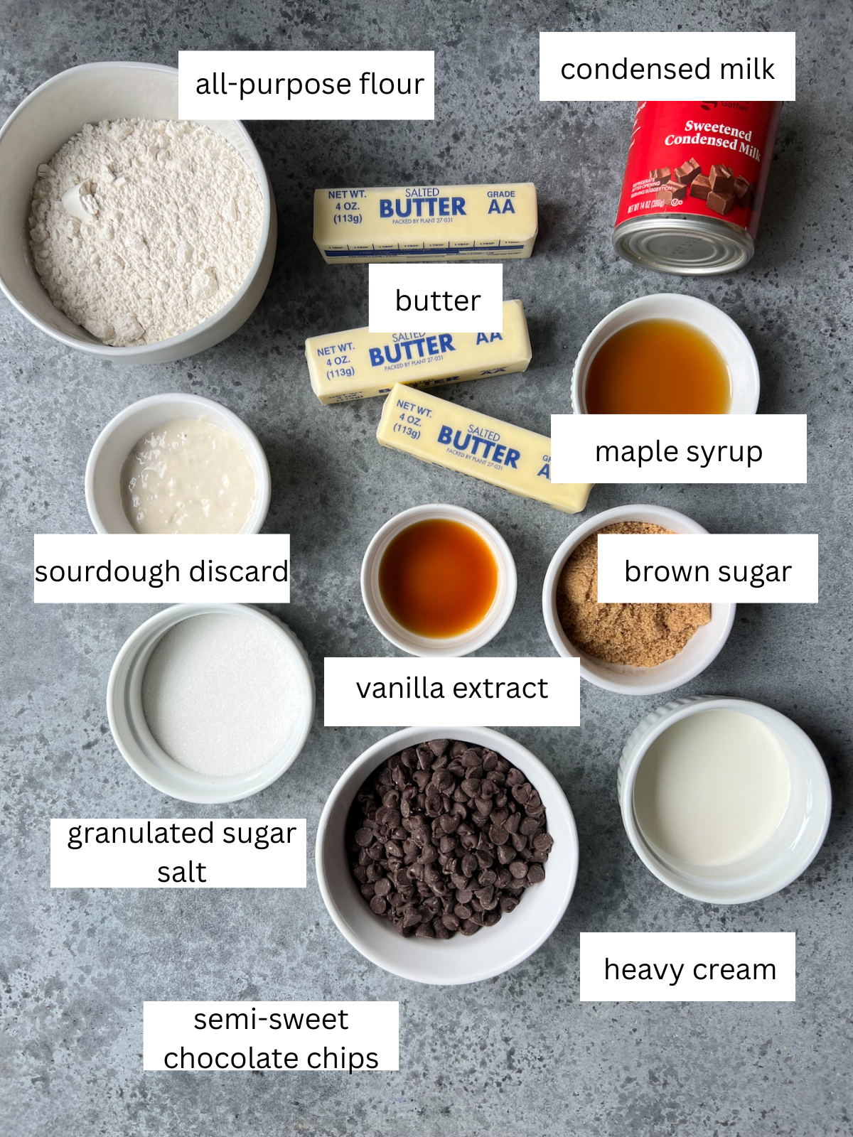 The ingredients needed for sourdough millionaire's shortbread: all-purpose flour, butter, condensed milk, sourdough discard, vanilla extract, maple syrup, brown sugar, heavy cream, granulated sugar, salt, semi-sweet chocolate chips.
