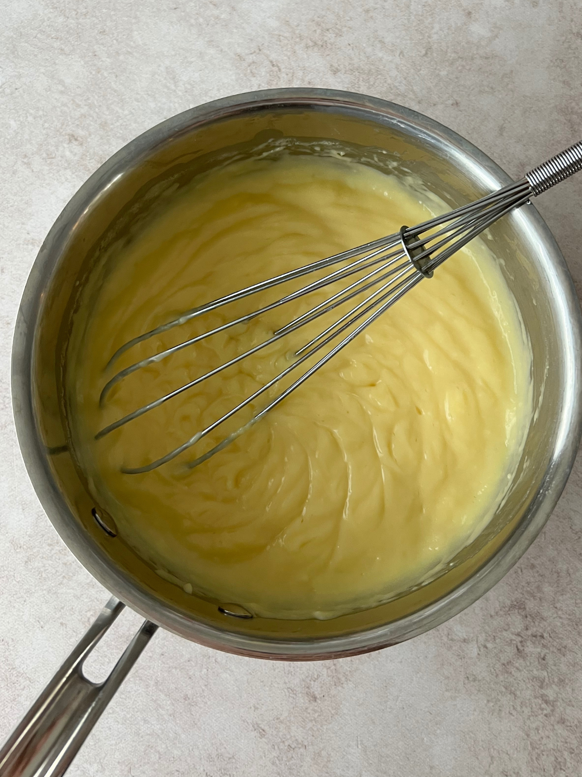 A saucepan with vanilla custard and a whisk in it.