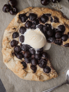 A rustic sourdough discard cherry cheesecake galette with a scoop of ice cream on top. One slice has been taken out of the galette.