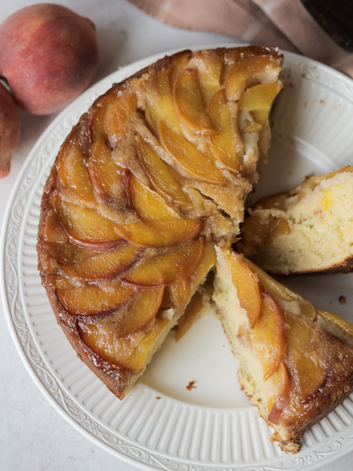 Peach upside down cake sits on a white plate with several slices cut out.
