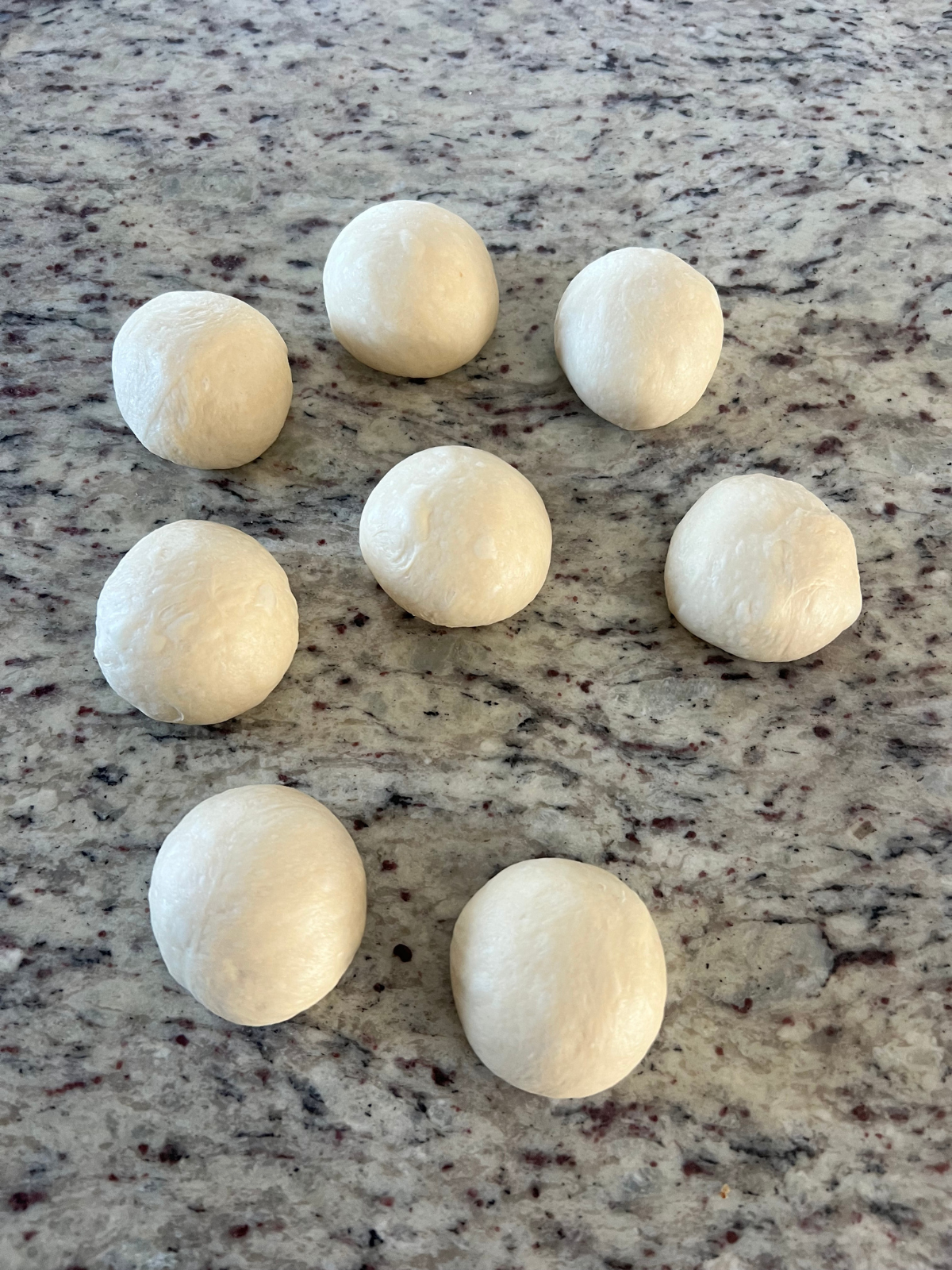 Eight pre-baked sourdough bagel dough balls sit on the counter.