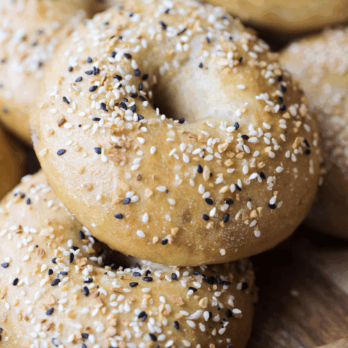 Several sourdough bagels sit on a wooden platter.