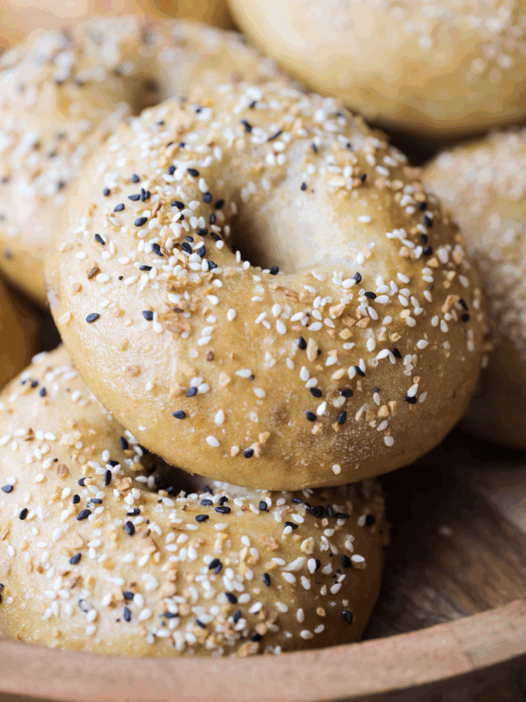 Several sourdough bagels sit on a wooden platter.