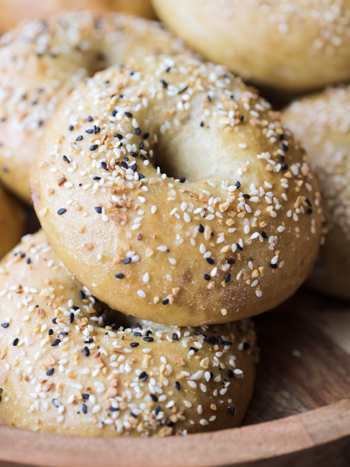 Homemade sourdough bagels with everything bagel seasoning on top. They are round, fluffy, and sitting on a wooden platter.