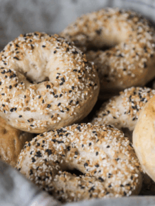 Several sourdough bagels with everything bagel seasoning on top of them. One bagel is shown close up.
