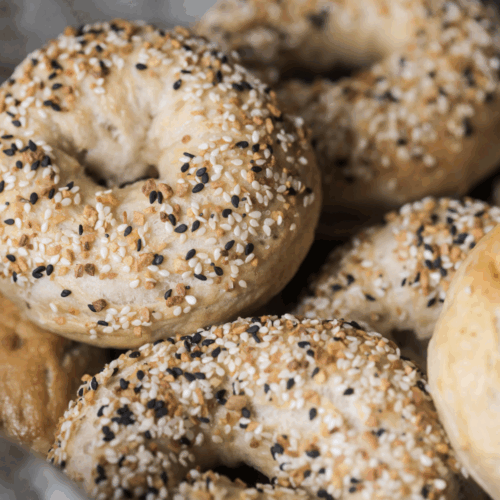 Several sourdough bagels with everything bagel seasoning on top of them. One bagel is shown close up.