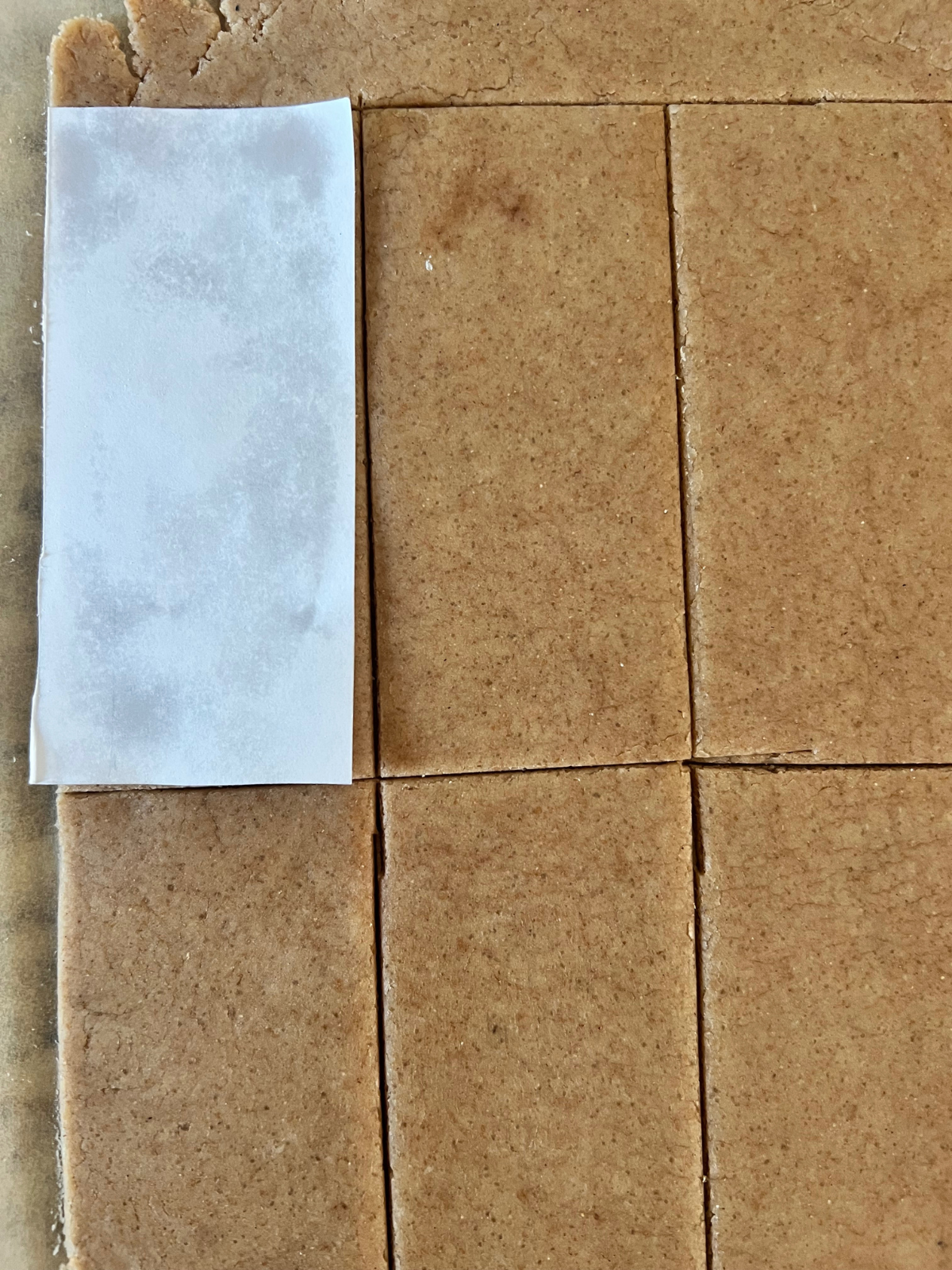 The sourdough graham cracker dough is rolled out and cut into rectangles. A 2x5 inch paper rectangle sits on top to show how to use it as a guide to make precise cuts. 
