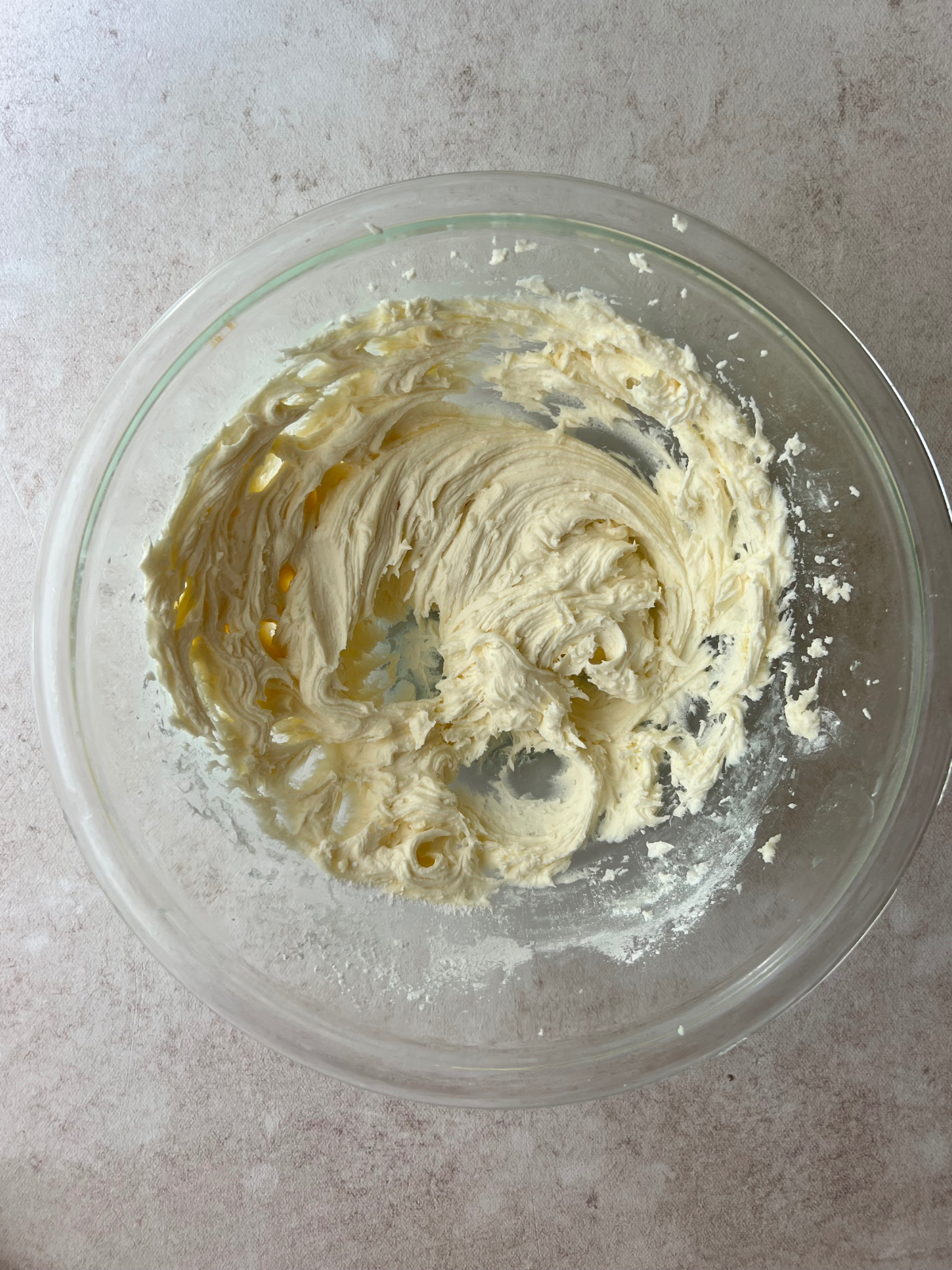A glass mixing bowl with vanilla buttercream frosting in it.