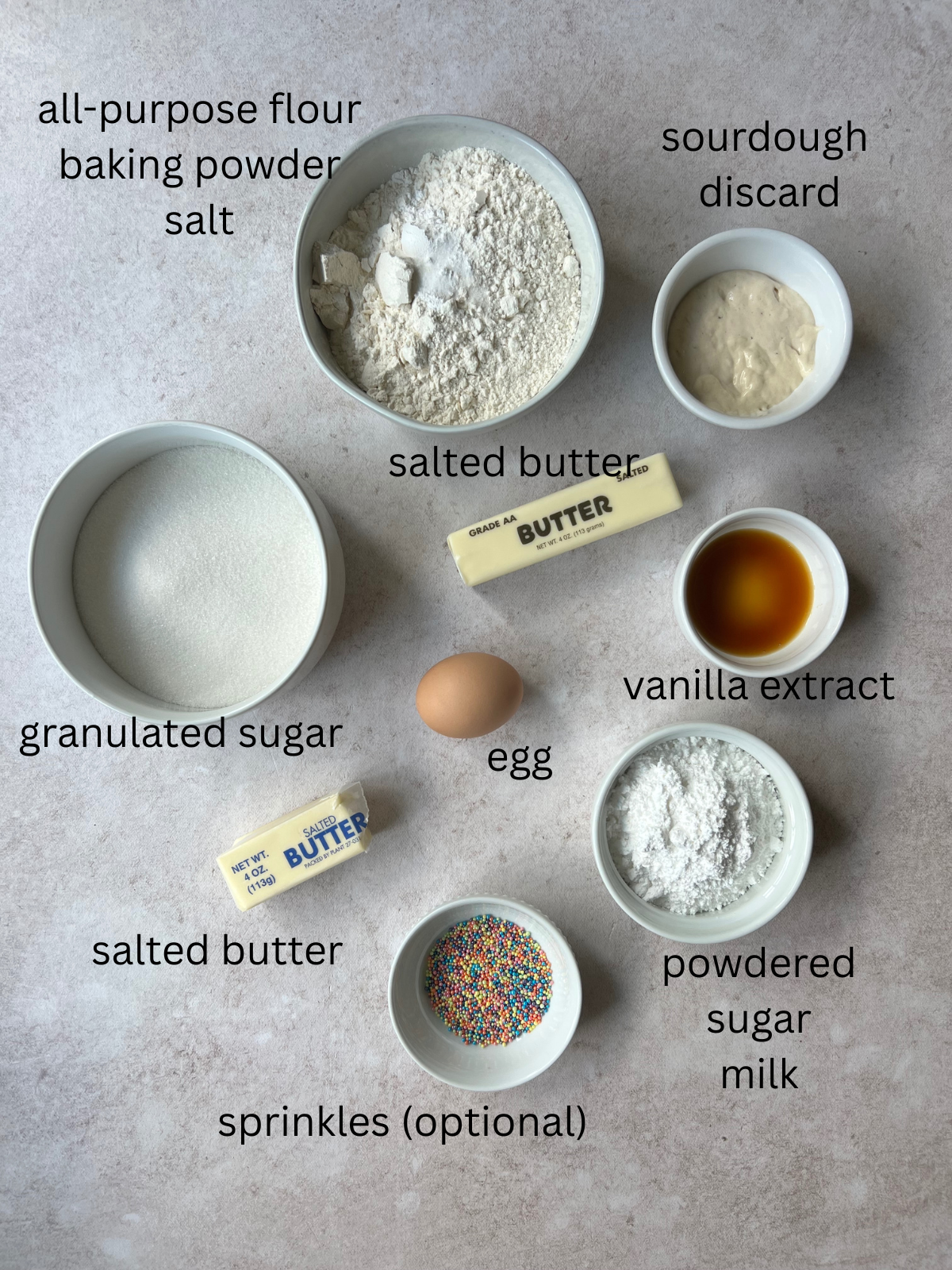 The ingredients for the sourdough sugar cookie bars: all-purpose flour, baking powder, salt, sourdough discard, salted butter, vanilla extract, granulated sugar, one egg, powdered sugar, and sprinkles. Not pictured is milk.