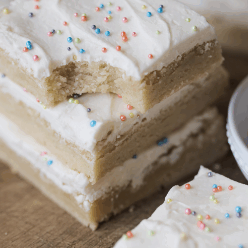 Three stacked sourdough sugar cookie bars on a wooden cutting board. One bar sits in front of them.