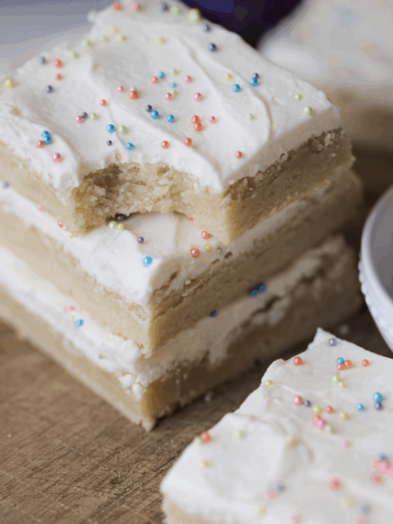 Three stacked sourdough sugar cookie bars on a wooden cutting board. One bar sits in front of them.