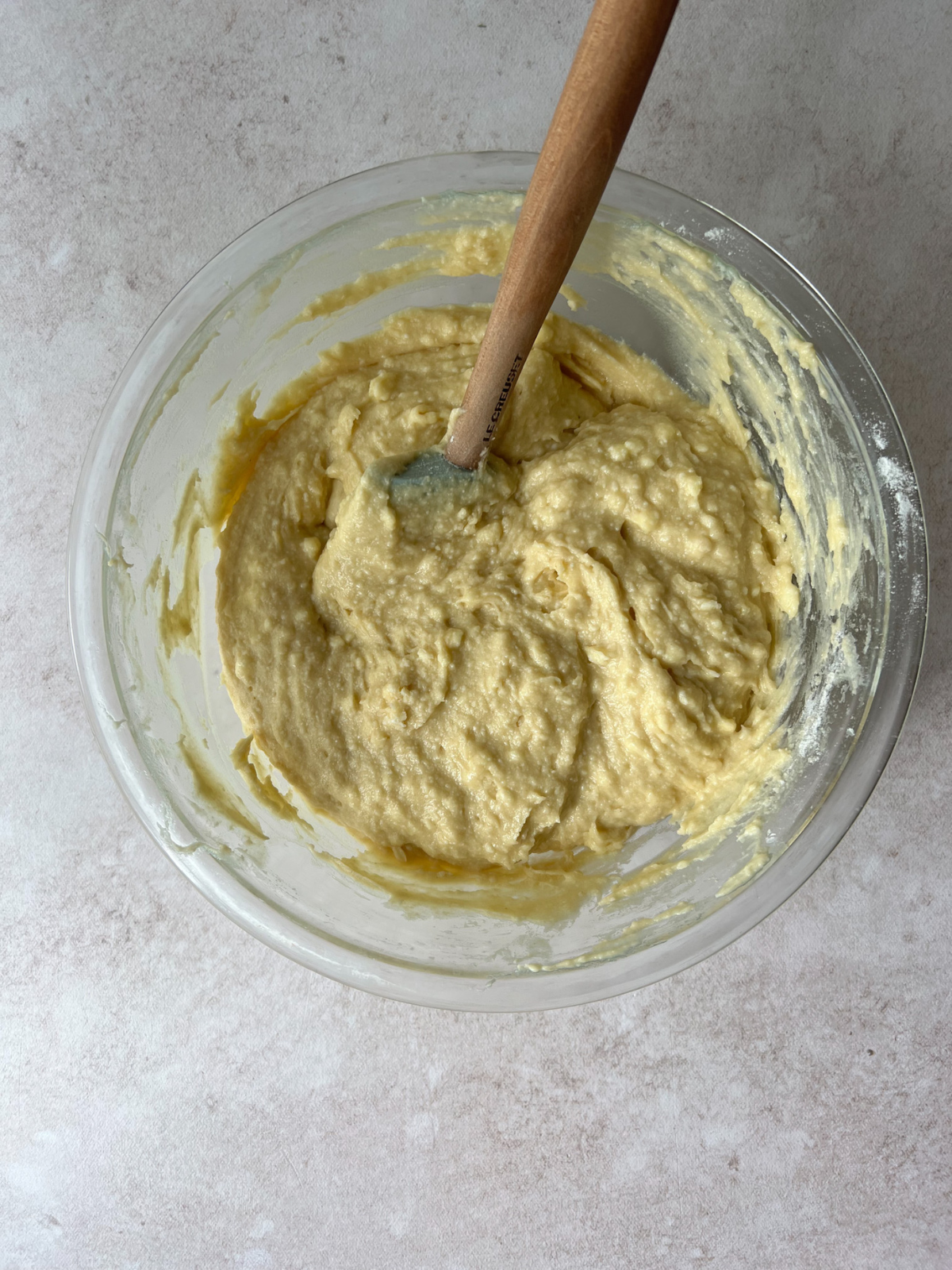 The ricotta cake batter sits in a glass mixing bowl. A rubber spatula sits in the bowl.