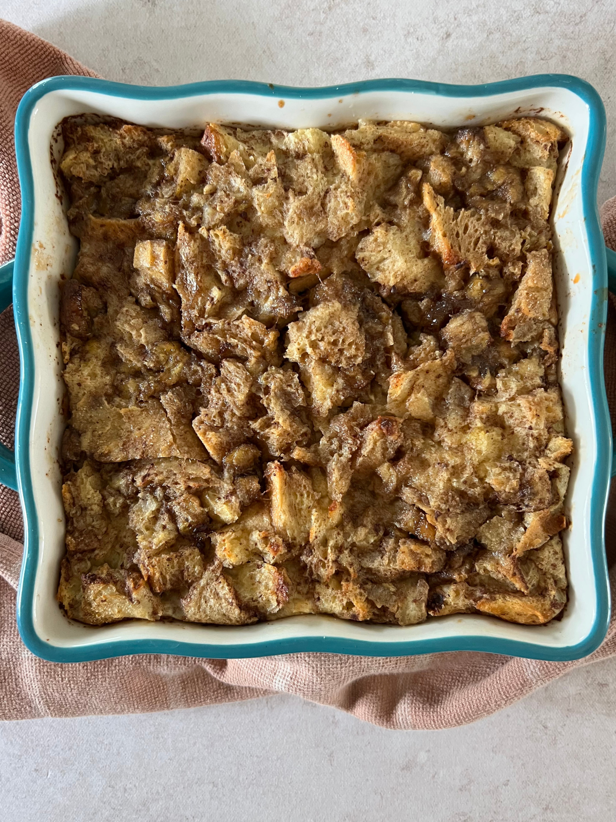 An 8x8 baking dish with the freshly baked sourdough bread pudding in it, sitting on the counter with a kitchen towel.