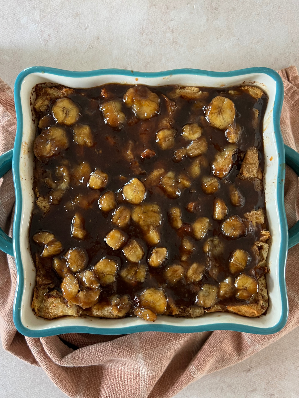 The baked sourdough bread pudding with bananas foster on top of the bread pudding in the 8x8 baking dish.