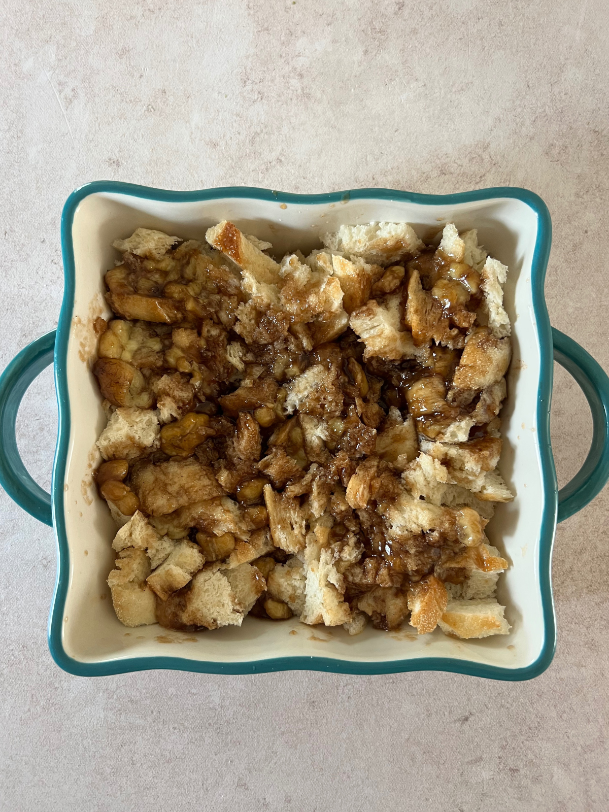An 8x8 baking dish with the torn sourdough bread pieces in it sit with the bananas foster on top.