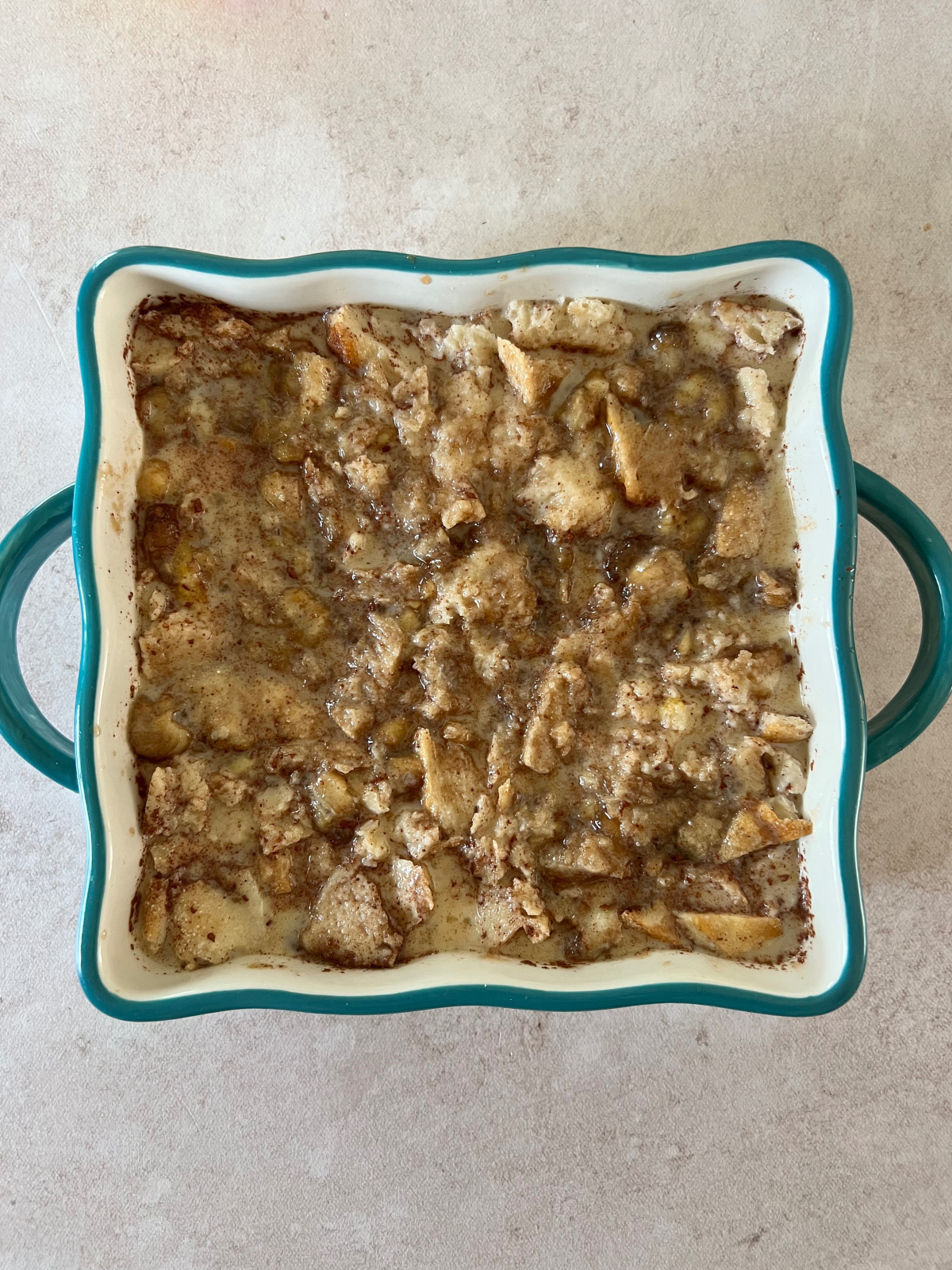 A picture of an 8x8 baking dish with prebaked bananas foster bread pudding with the custard on the bread pieces. 