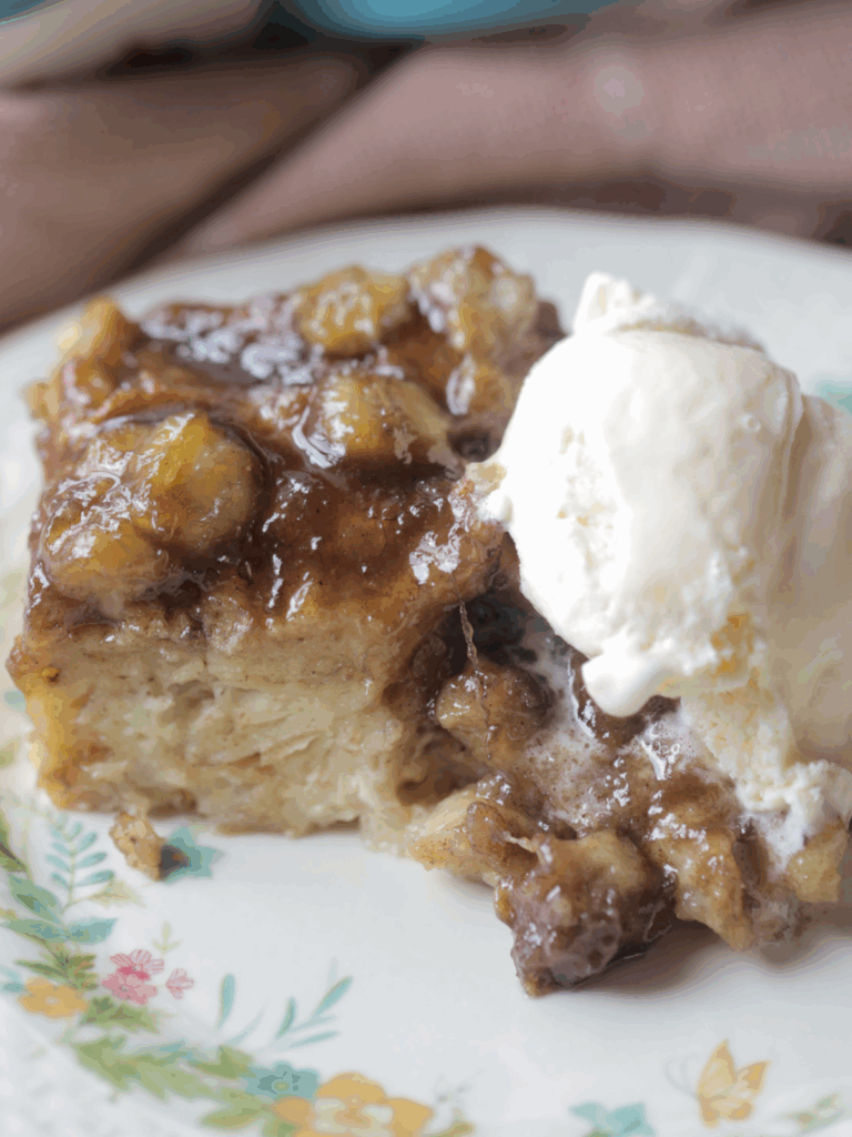 A closeup of a serving of bananas foster bread pudding with a scoop of vanilla ice cream.