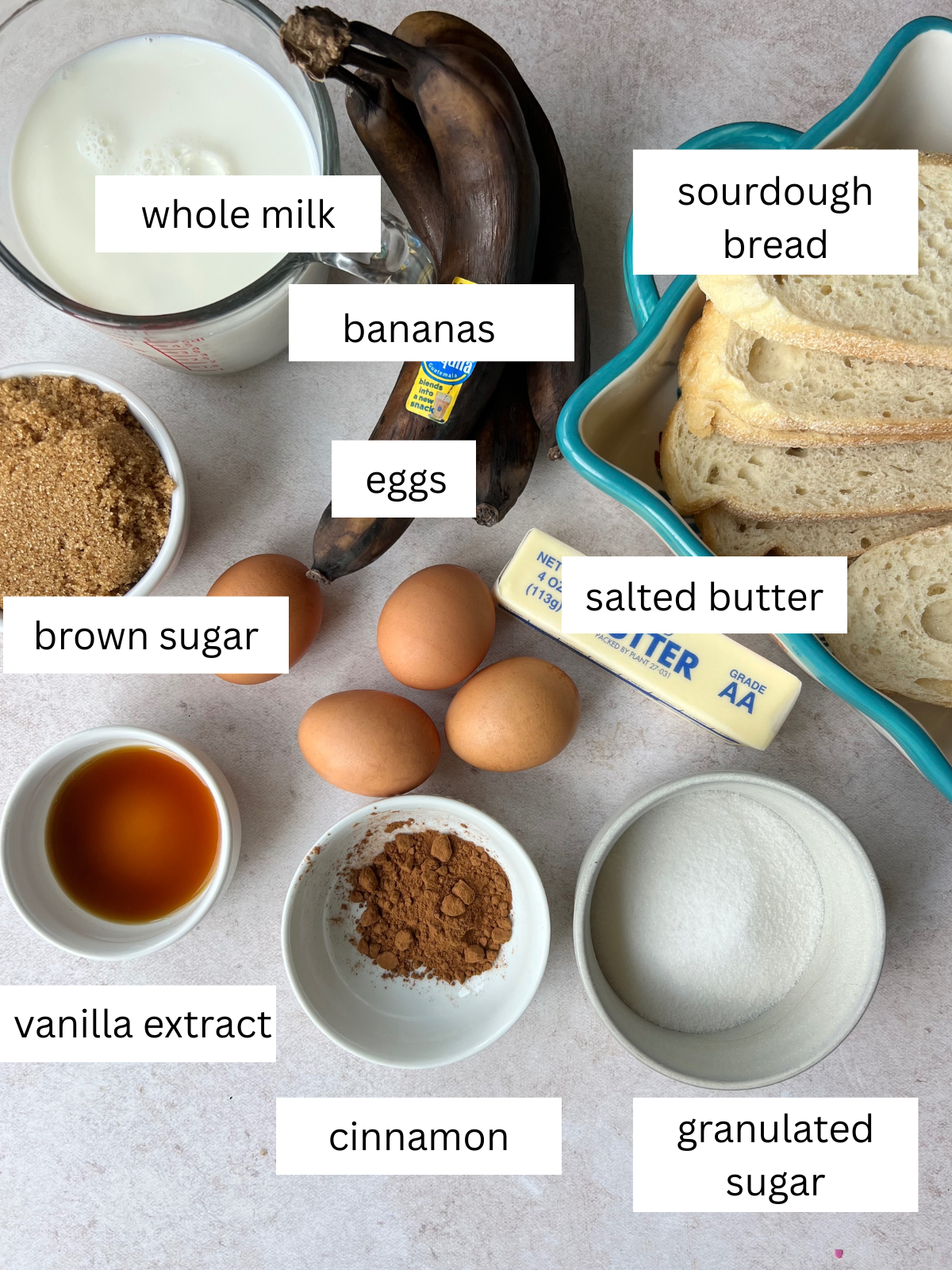 Ingredients for the Bananas Foster Bread Pudding: bananas, granulated sugar, ground cinnamon, vanilla extract, salted butter, eggs, whole milk, brown sugar, and sourdough bread slices.