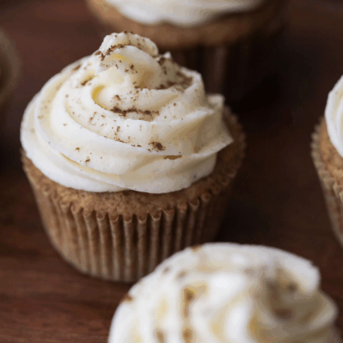 Closeup of one sourdough pumpkin cupcake with cream cheese frosting with a few others in the background and foreground.