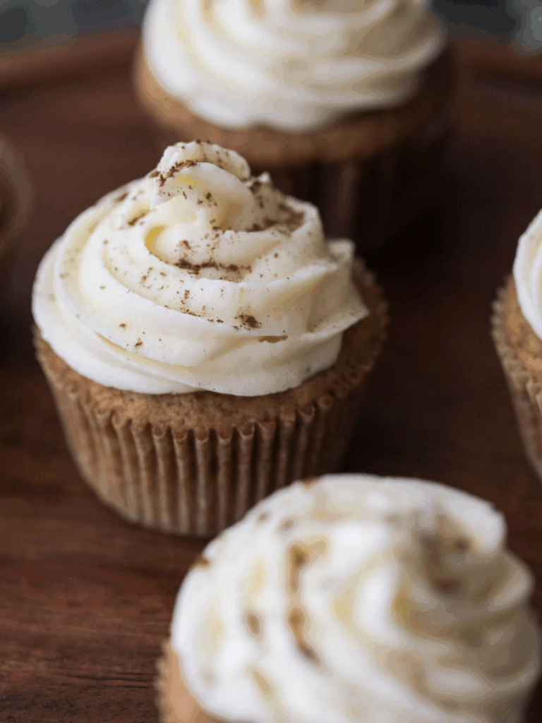 Closeup of one sourdough pumpkin cupcake with cream cheese frosting with a few others in the background and foreground.