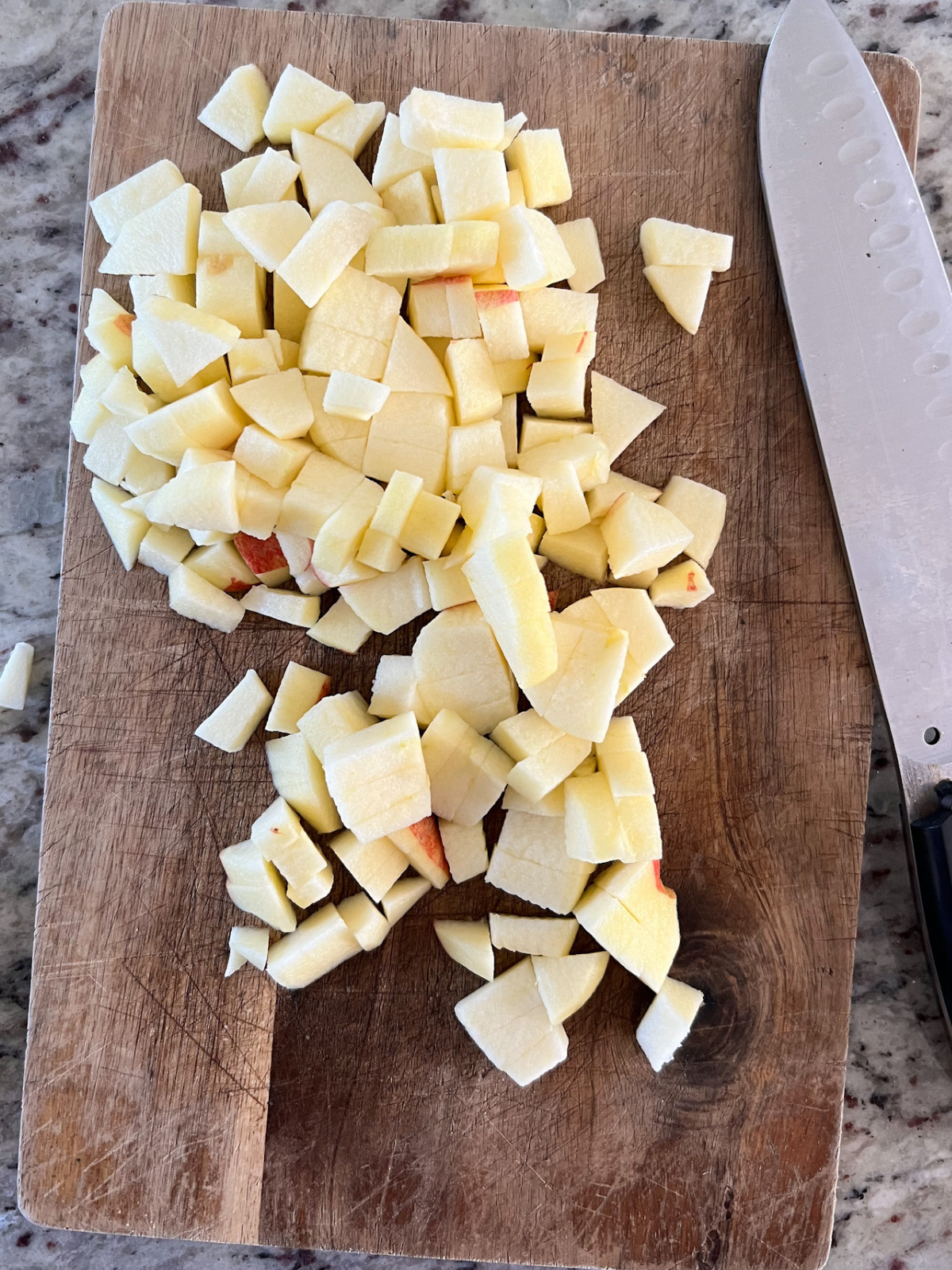Cubed apples sit on a wooden cutting board with a knife to the side.