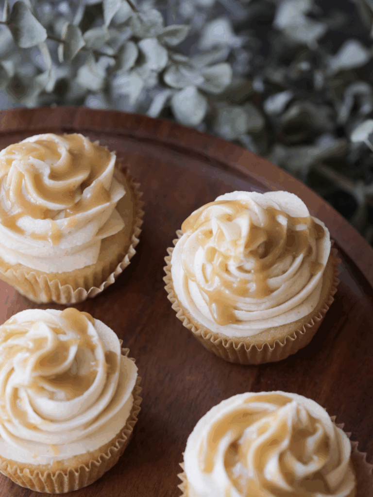 Several brown butter salted caramel cupcakes with brown butter salted caramel cream cheese frosting. Caramel is drizzled over the cupcakes.
