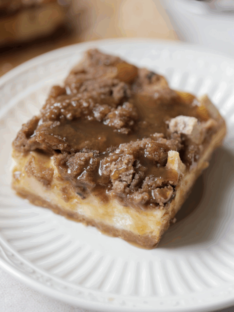 One caramel apple cheesecake bar sits on a plate. Caramel is drizzled over the bar.