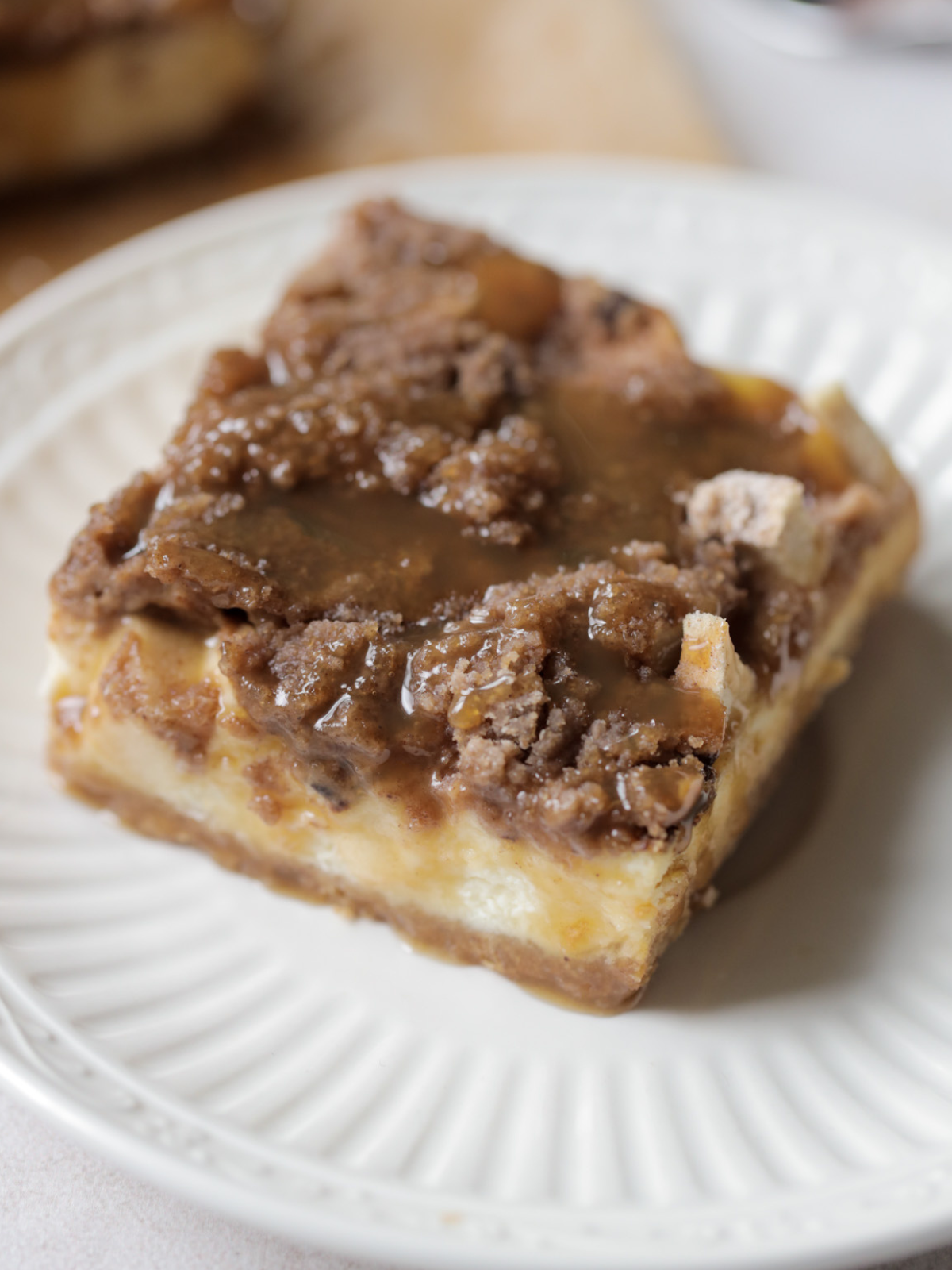 One caramel apple cheesecake bar sits on a plate. Caramel is drizzled over the bar.
