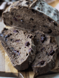A loaf of cherry chocolate sourdough bread is cut in half in the background while two slices of the bread sit in the foreground.