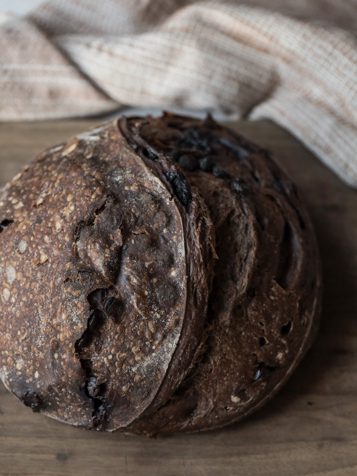A full chocolate cherry sourdough loaf sits on a wooden cutting board.