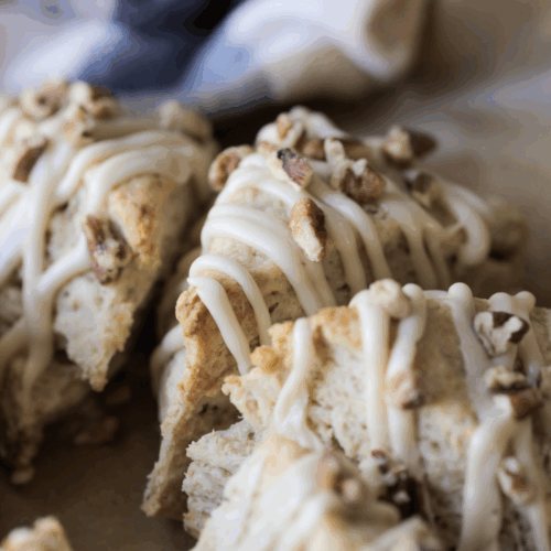 A closeup of three sourdough maple pecan scones with maple icing drizzled on top.