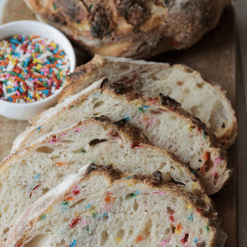 Four slices of funfetti and white chocolate sourdough bread with a bowl of sprinkles and the other half of the loaf in the background.