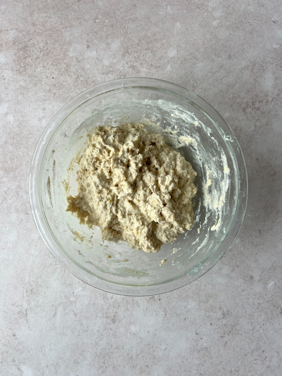 A glass mixing bowl sits on the counter with shaggy sourdough bread dough in it.