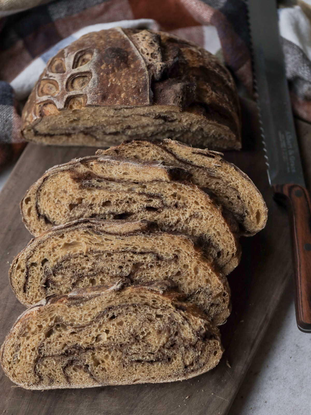 A sliced loaf of sourdough pumpkin swirl bread sits on a wooden cutting board. A serrated bread knife sits to the side of the cutting board.