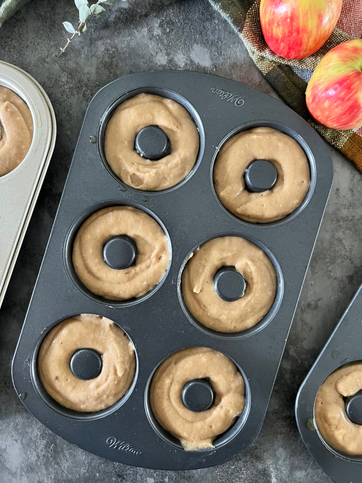 A donut pan sits on the counter with sourdough apple cider donut batter in it. 