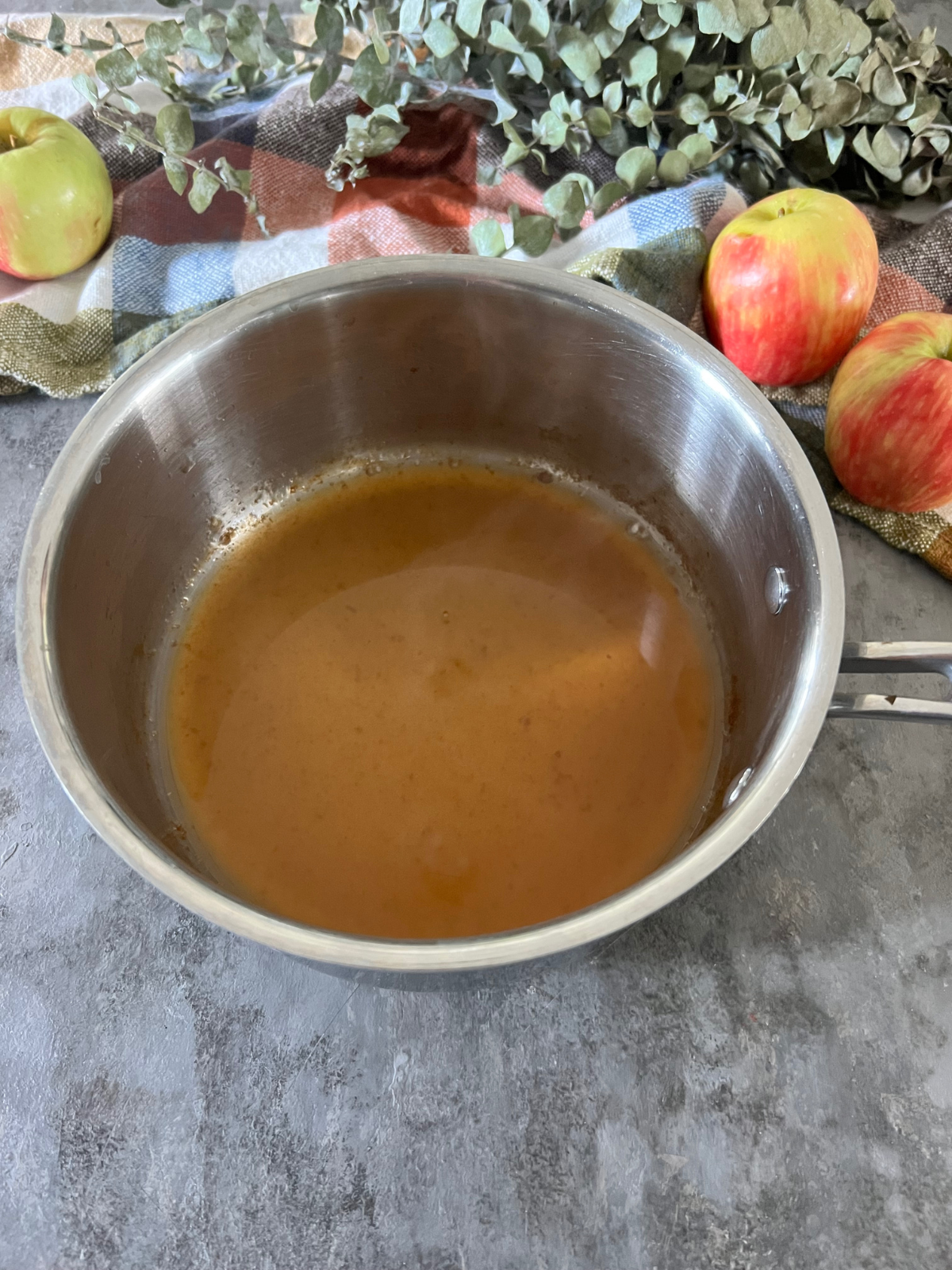 Reduced apple cider for the sourdough apple cider doughnuts in a saucepan sits on the counter.