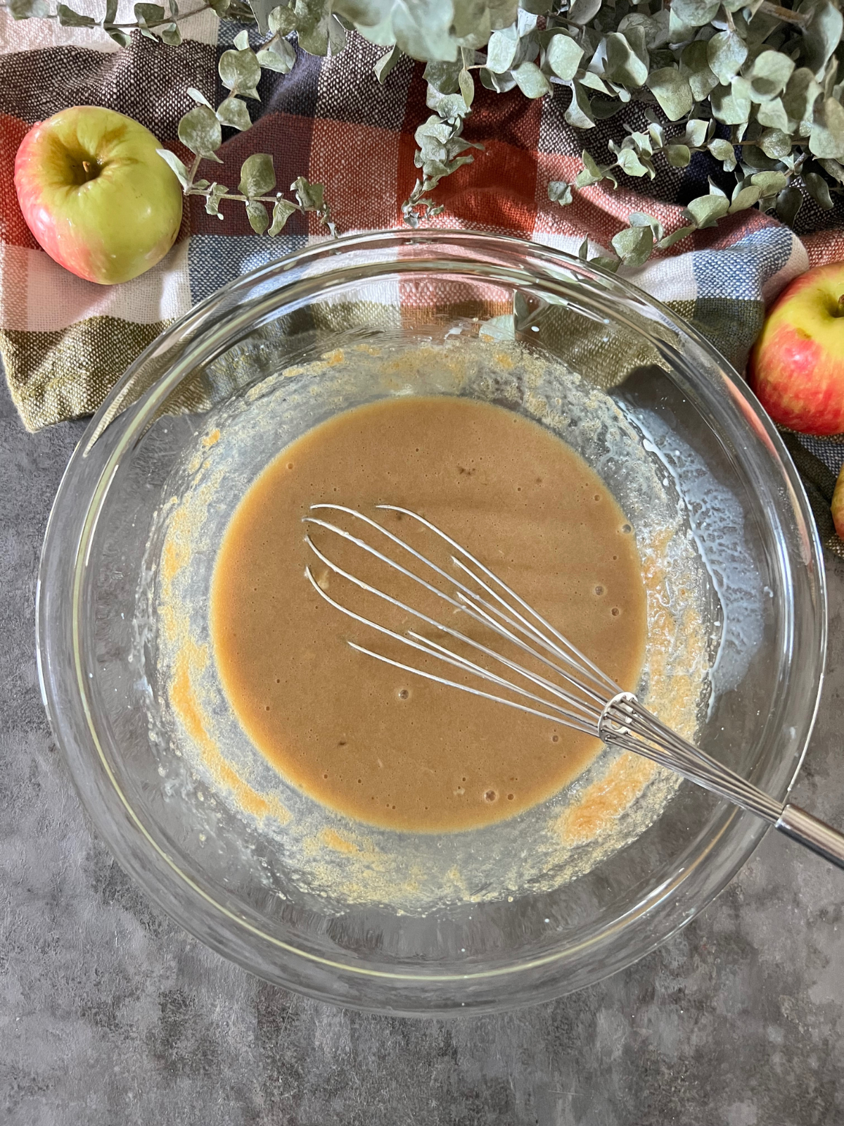 A glass mixing bowl with a whisk in it sits with the wet ingredients for the sourdough apple cider donuts.
