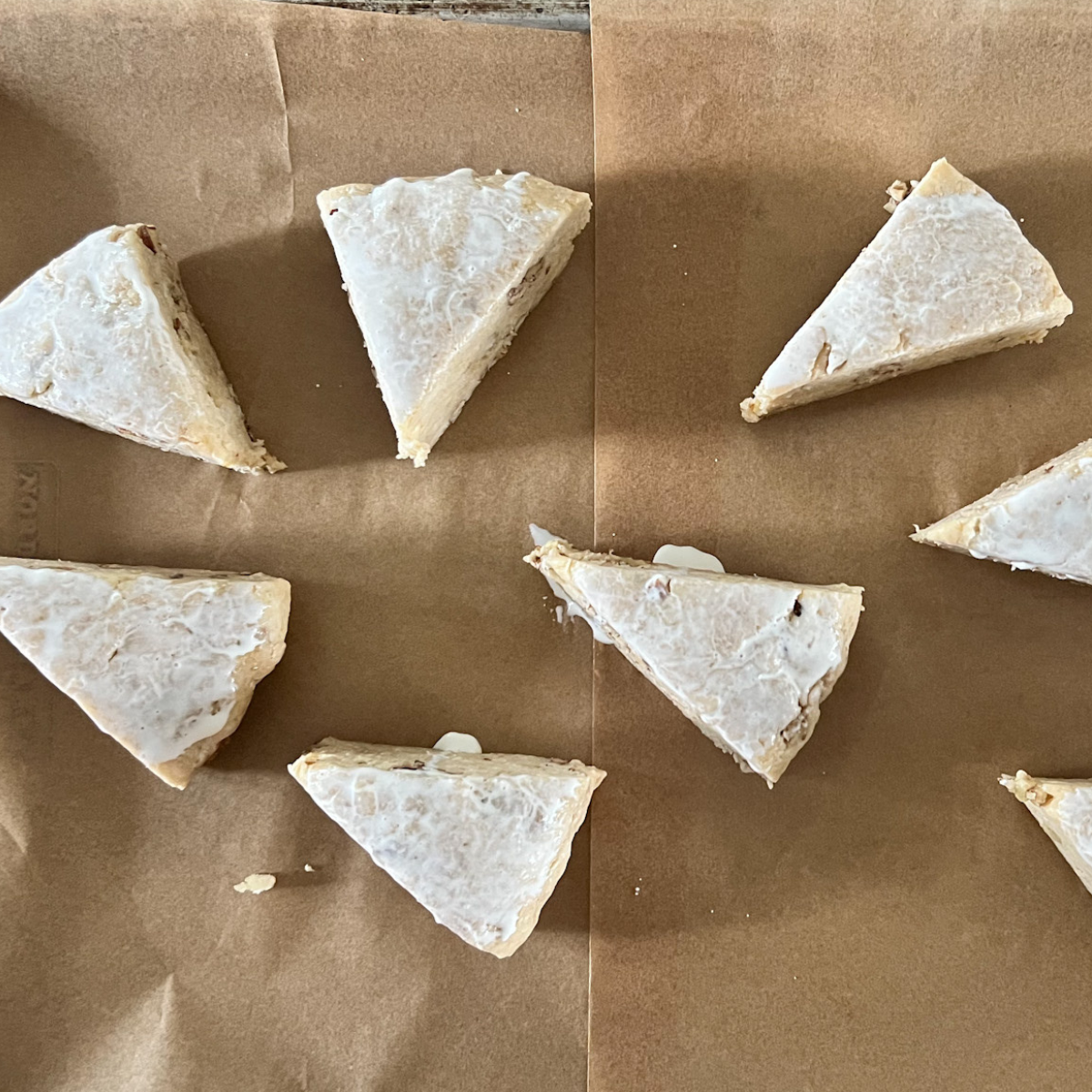 Unbaked sourdough maple pecan scones sit on a parchment-lined baking sheet with heavy cream brushed over them. 