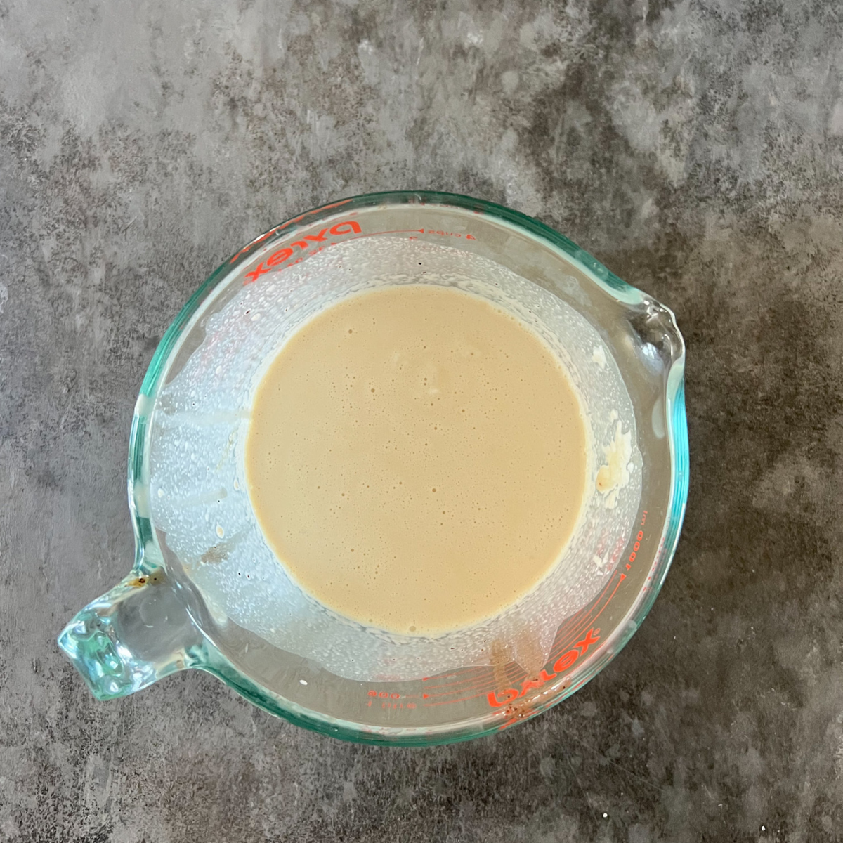 A large measuring cup holds the wet ingredients for the maple pecan sourdough scones: egg, sourdough discard, heavy cream, and vanilla extract. 