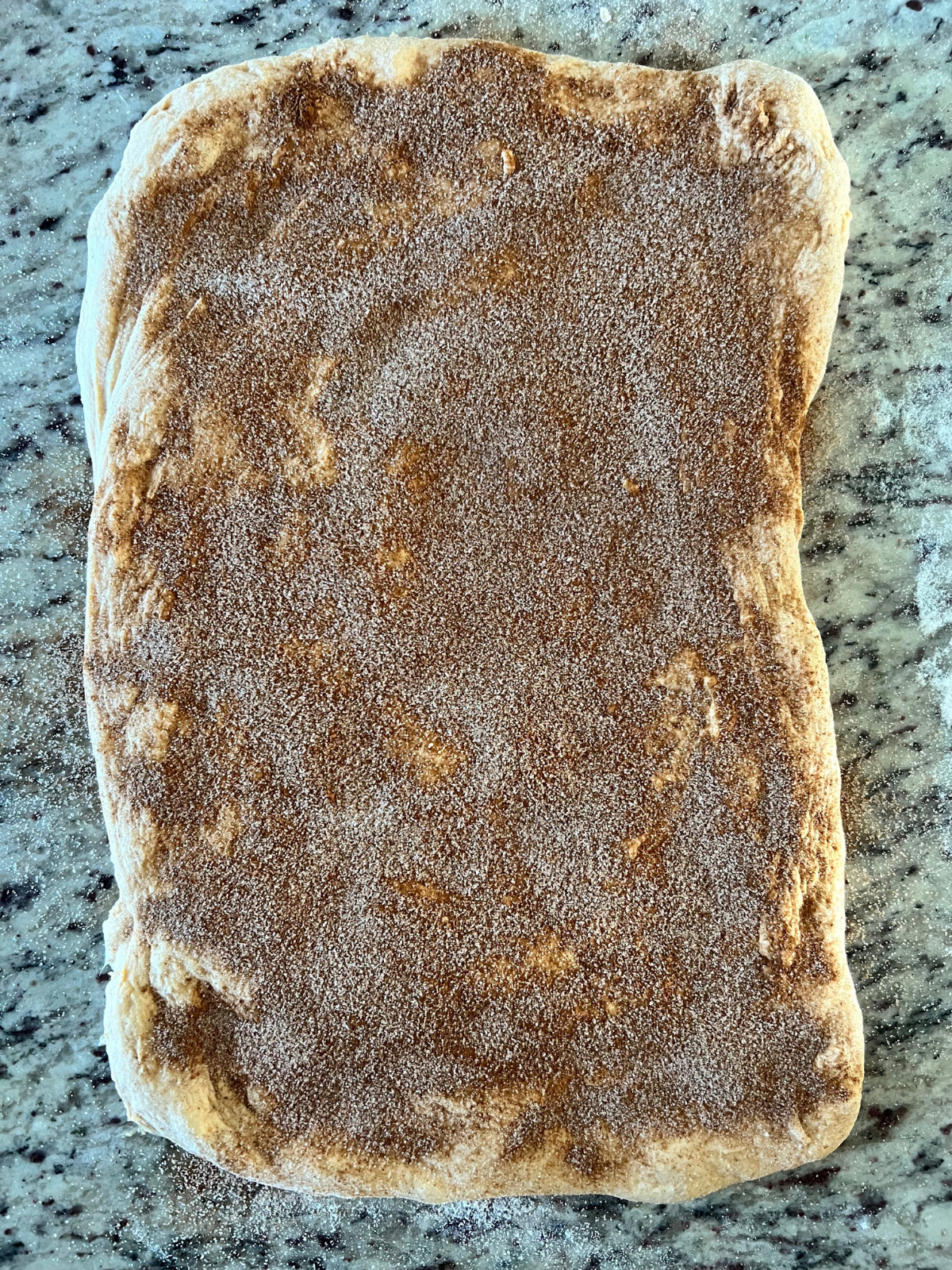 The dough is stretched out into a rectangle with cinnamon and sugar sprinkled over the surface.