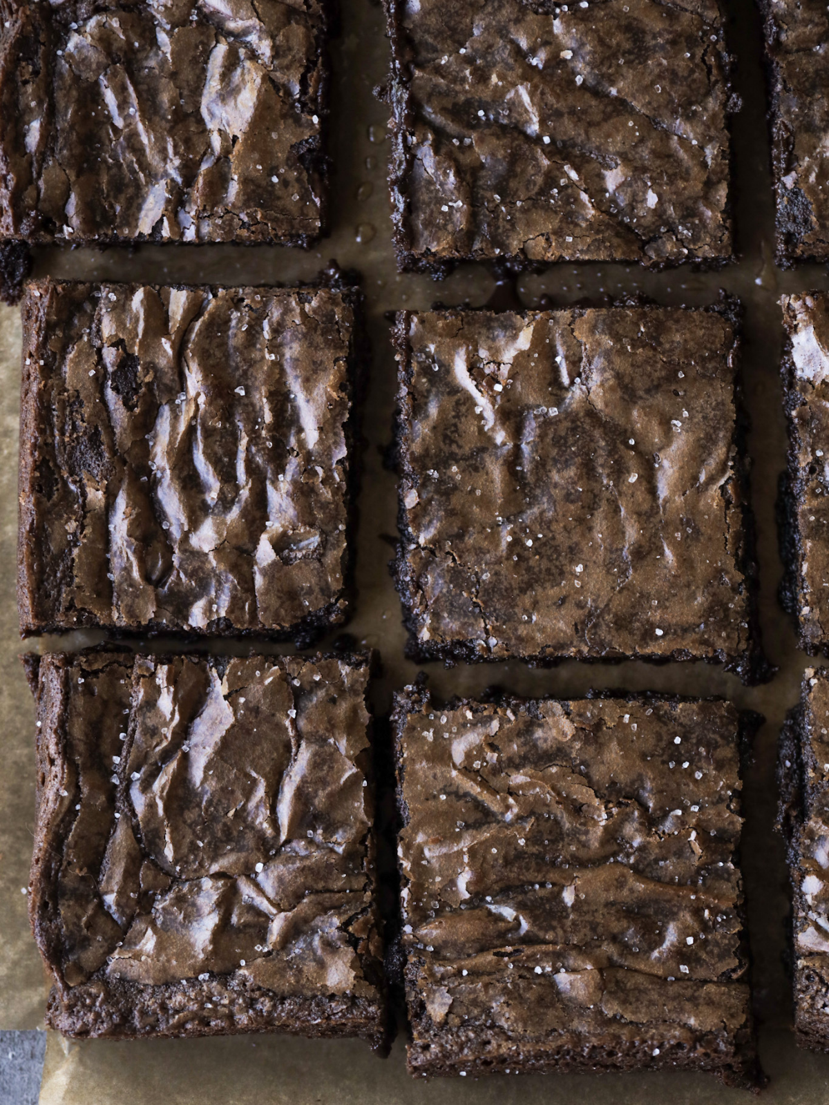 Six brown butter brownie squares sit on parchment paper.