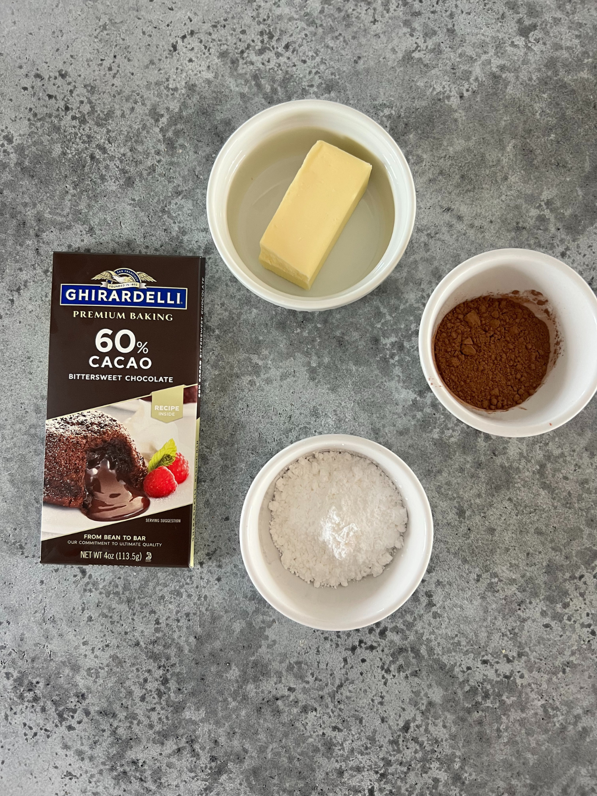 The bittersweet chocolate, butter, cocoa powder, and powdered sugar sit on the counter. They will be used to make the chocolate filling for the sourdough babka.