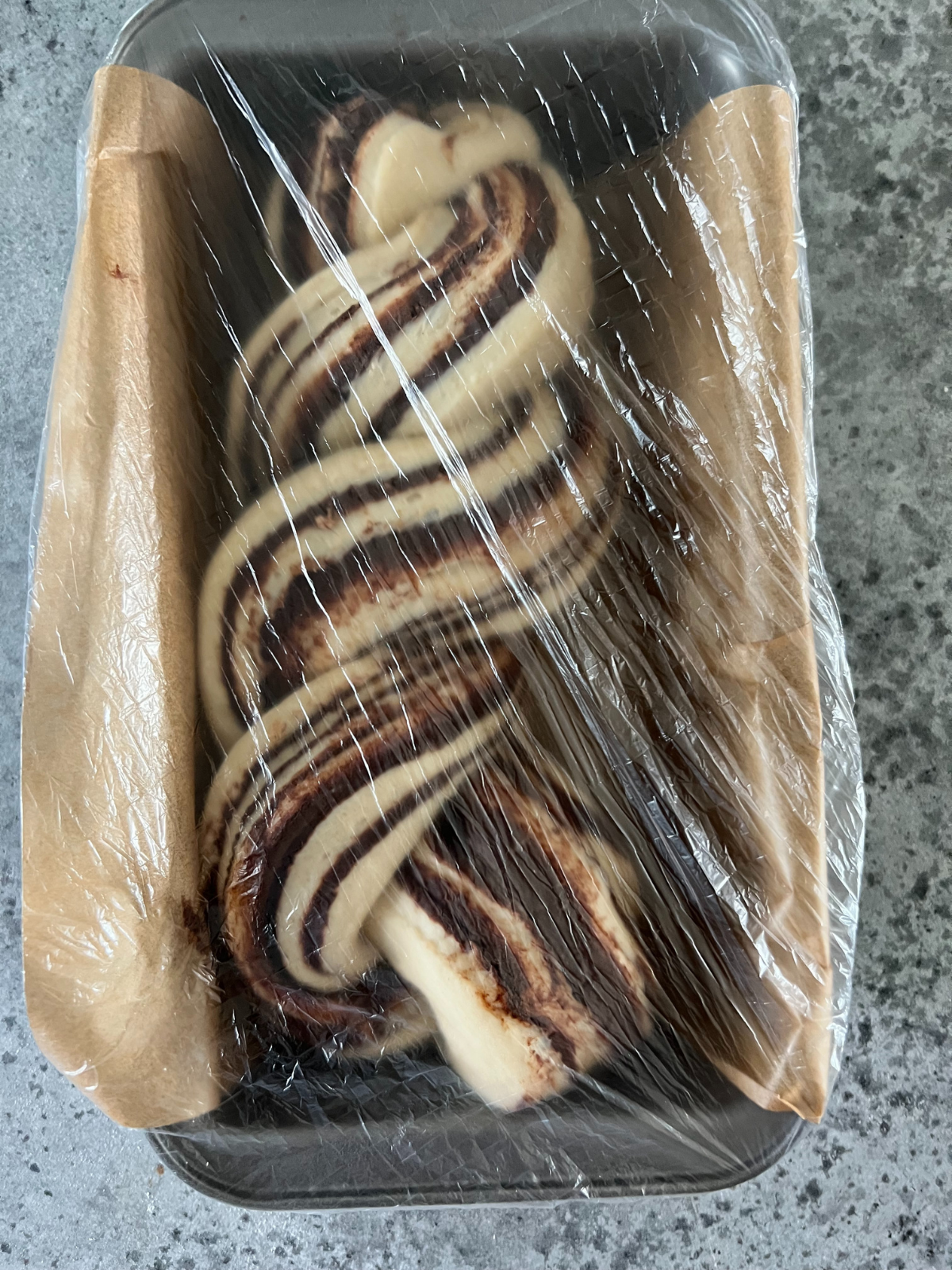 The enriched braided dough has been transferred to a parchment-lined loaf pan and covered, to allow it to have its second rise.