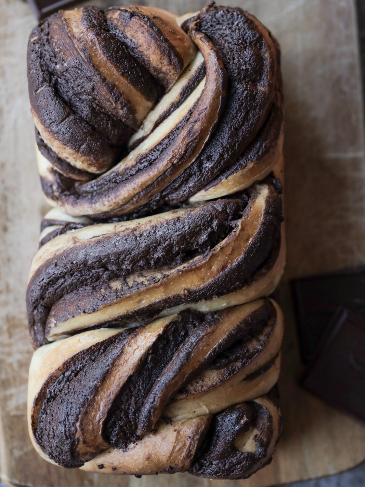 A loaf of freshly baked sourdough chocolate babka sits on a cutting board.